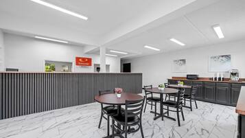 A modern hotel lobby with a reception desk, a dining area with marble flooring, and a kitchen area with dark cabinetry.