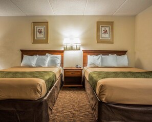 Una habitación de hotel con dos camas, una mesita de noche y una lámpara fijada a la pared.