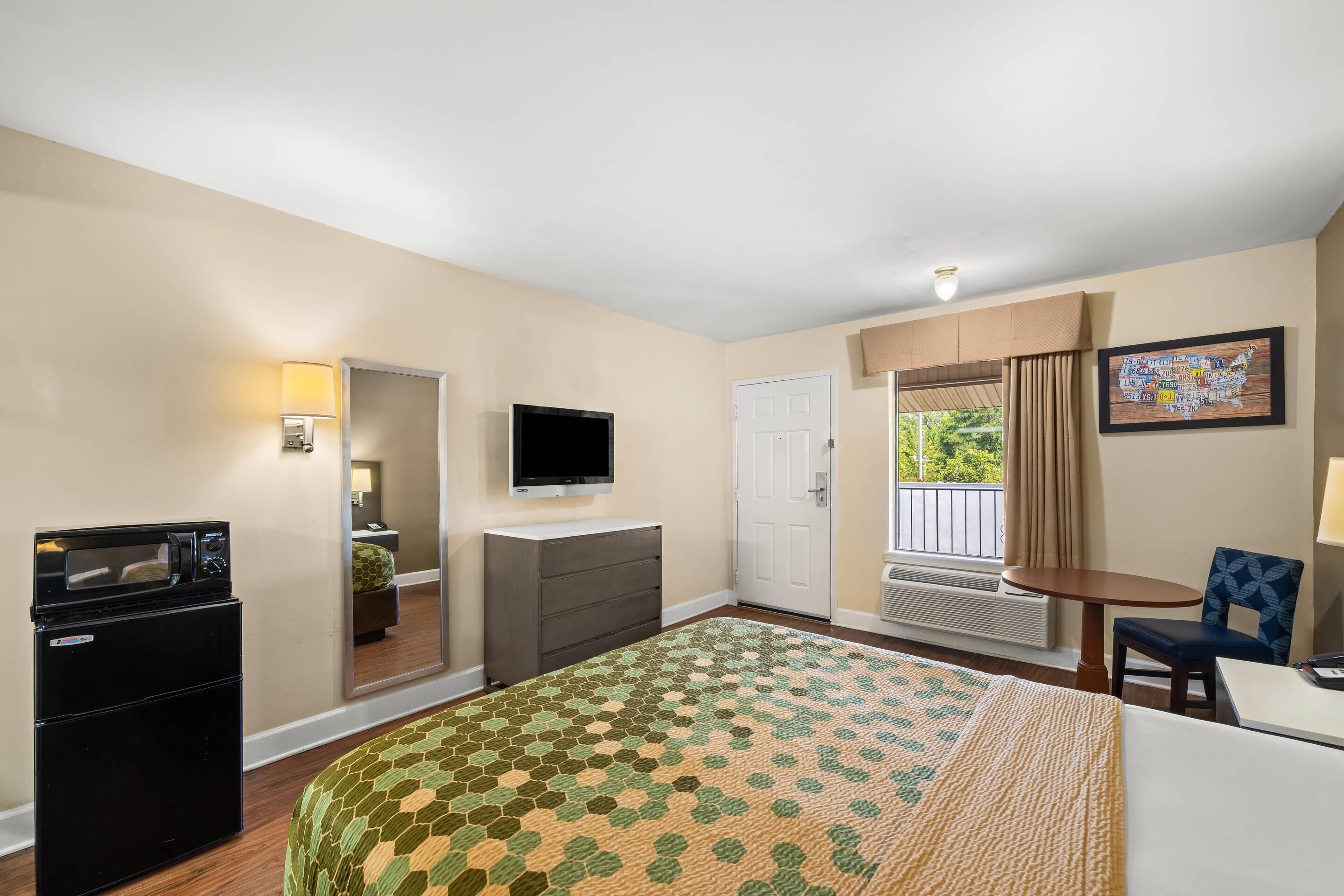 A hotel room with a bed, a desk, a TV, a mini-fridge, and a window with curtains.