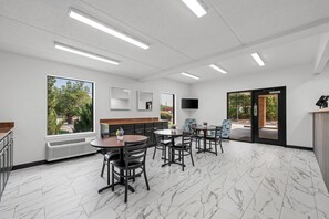 A modern interior with a marble floor, a dining area with tables and chairs, a large window with a view of trees, and a flat-screen TV mounted on the wall. - Econo Lodge Inn & Suites Lugoff (Lugoff)