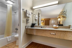Un baño con bañera, inodoro, lavamanos y un espejo grande.
