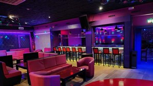 Un espace lounge moderne avec des sièges rouges, un bar avec des tabourets et un éclairage d’ambiance.