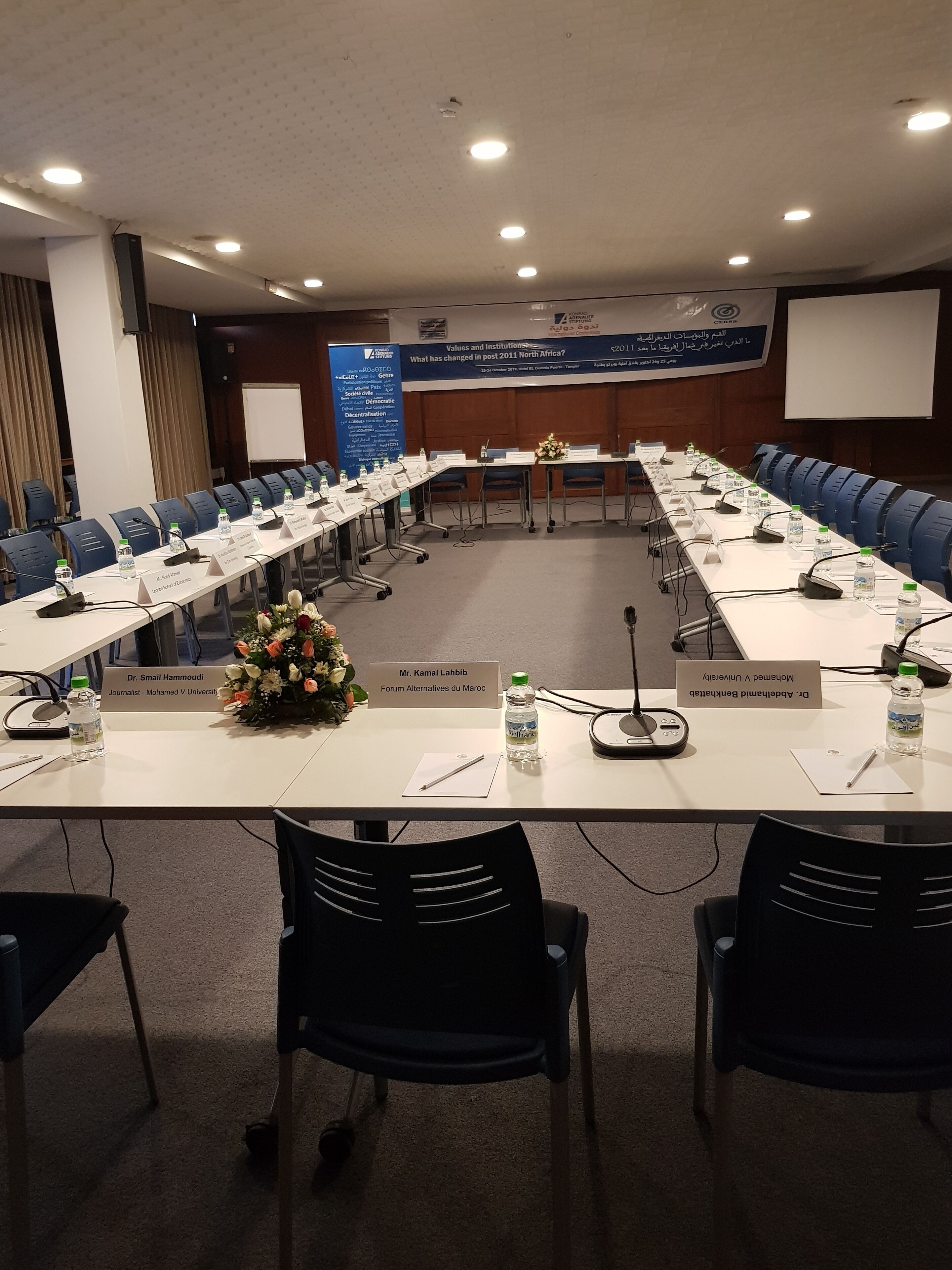 A conference room with a long table, nameplates, microphones, and water bottles.