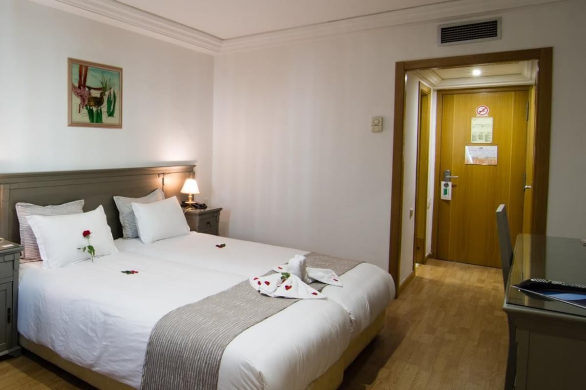 Une chambre d’hôtel avec un lit bien fait, une table de chevet avec une lampe et une porte sur laquelle est apposée une pancarte.