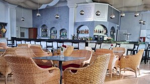 Een ruime, overdekte eethoek met rieten stoelen en een bar op de achtergrond.