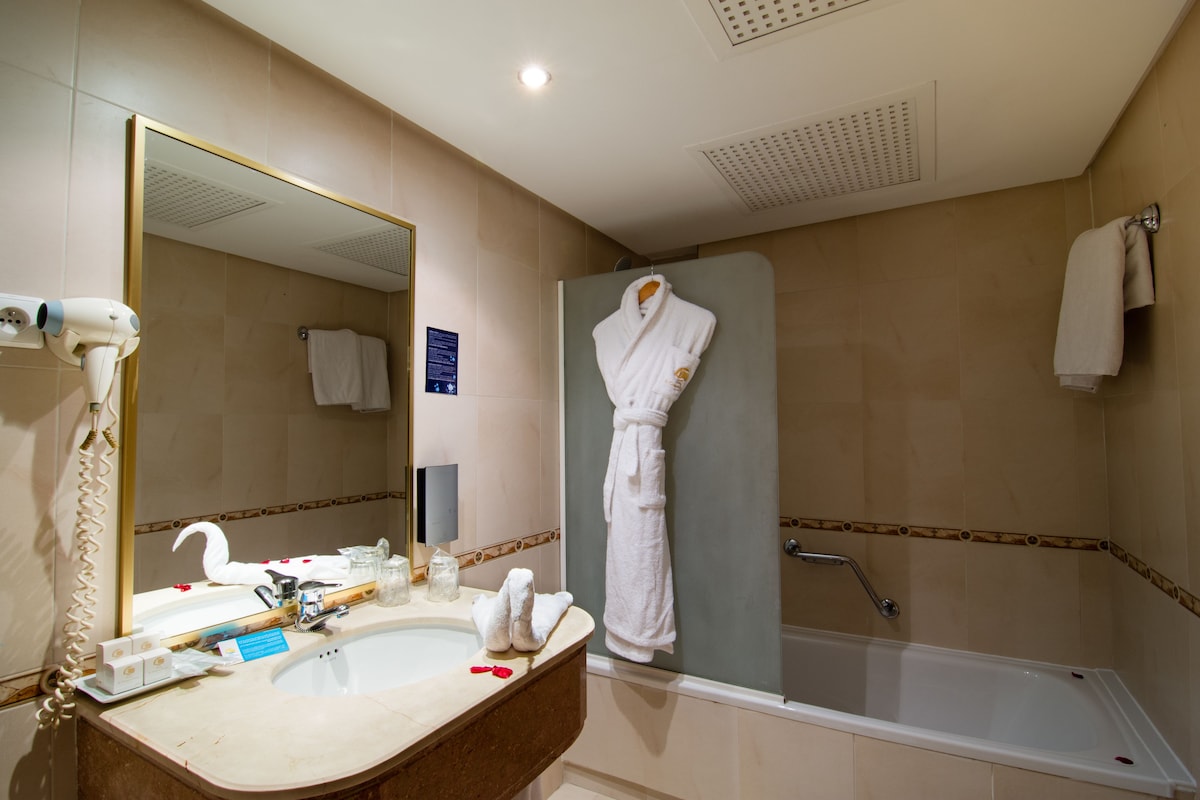 Une salle de bain équipée d’un lavabo, d’un miroir, d’un peignoir et d’une douche.