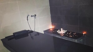 Une salle de bain aux carreaux noirs, avec un miroir, un porte-serviettes et une petite étagère sur laquelle sont posées des bougies.