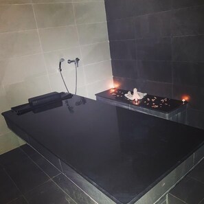 Een badkamer met zwarte tegels, een spiegel, een handdoekhouder en een klein plankje met kaarsen.
