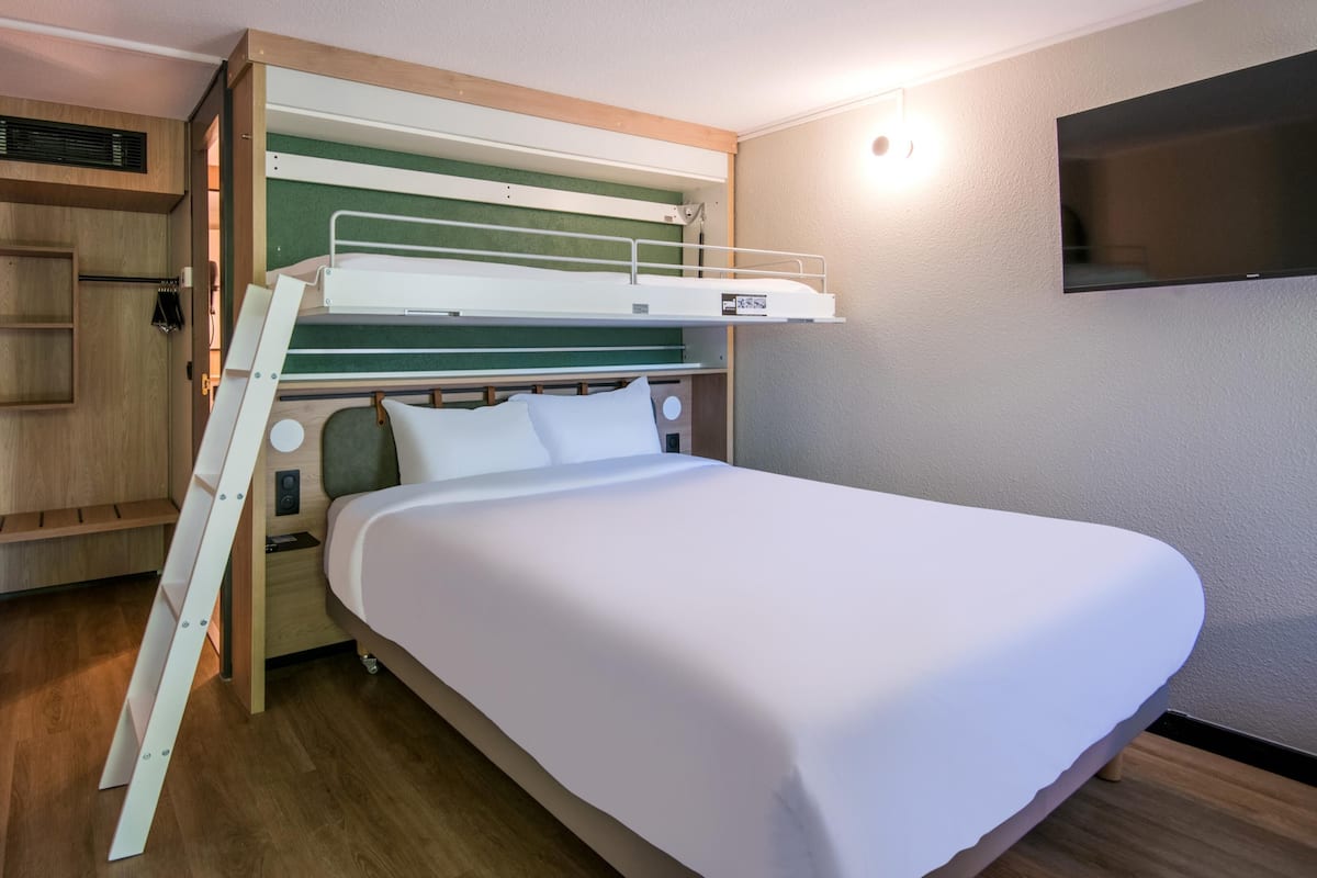 A bunk bed with a wooden ladder, a small shelf, and a television on the wall.