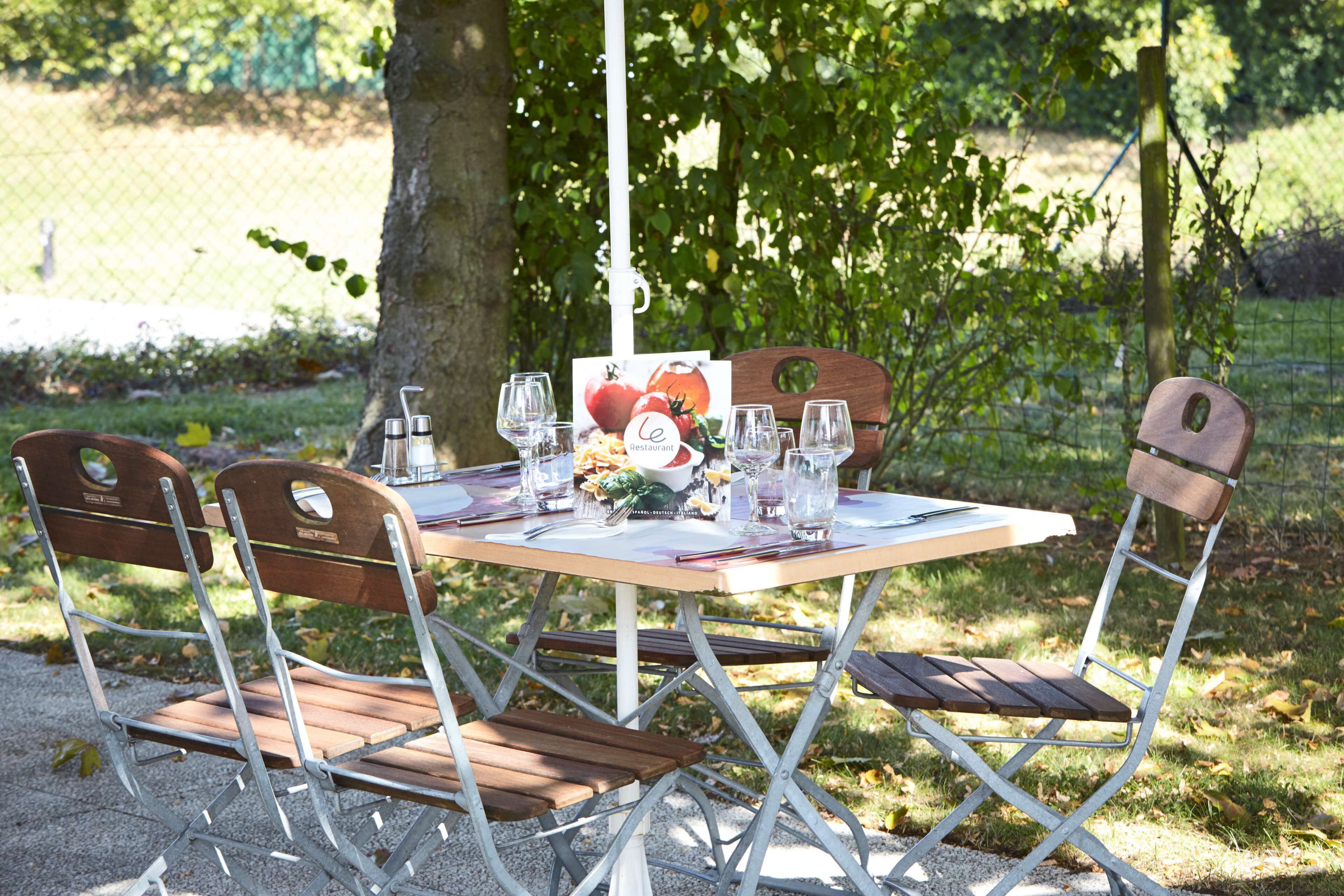 Una mesa dispuesta al aire libre con sillas de metal, mantel blanco y una carta.