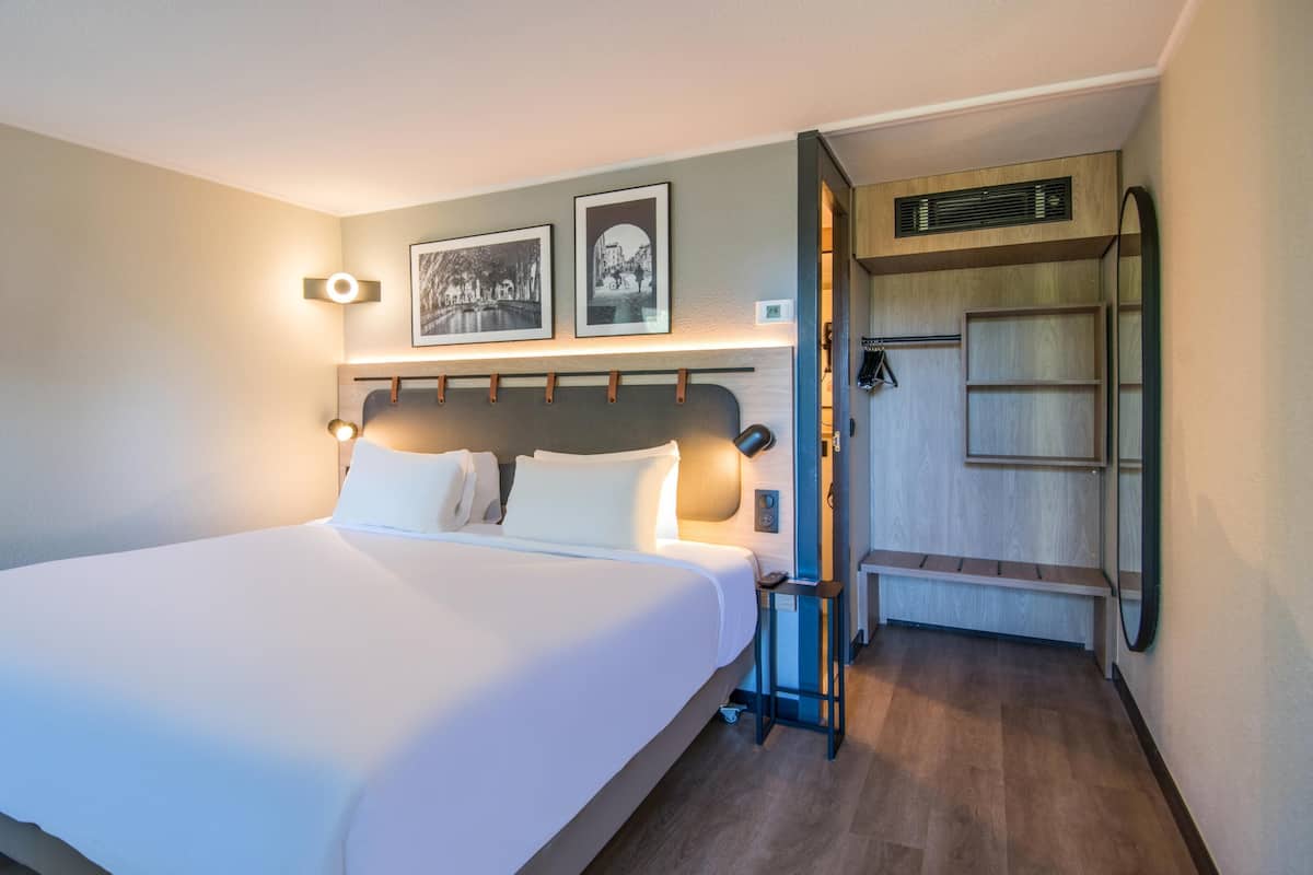 A hotel room with a large bed, a flat-screen TV mounted on the wall, and a wooden bench in the corner.