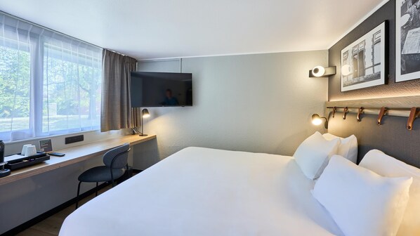 A hotel room with a large bed, a desk with a chair, a television, and a window with curtains.