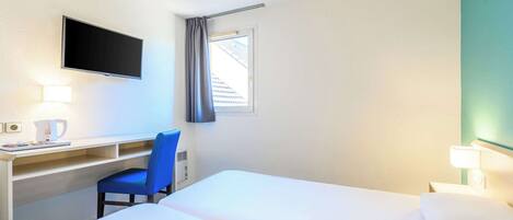 Una habitación de hotel con cama, escritorio, silla, televisor y ventana con cortinas.