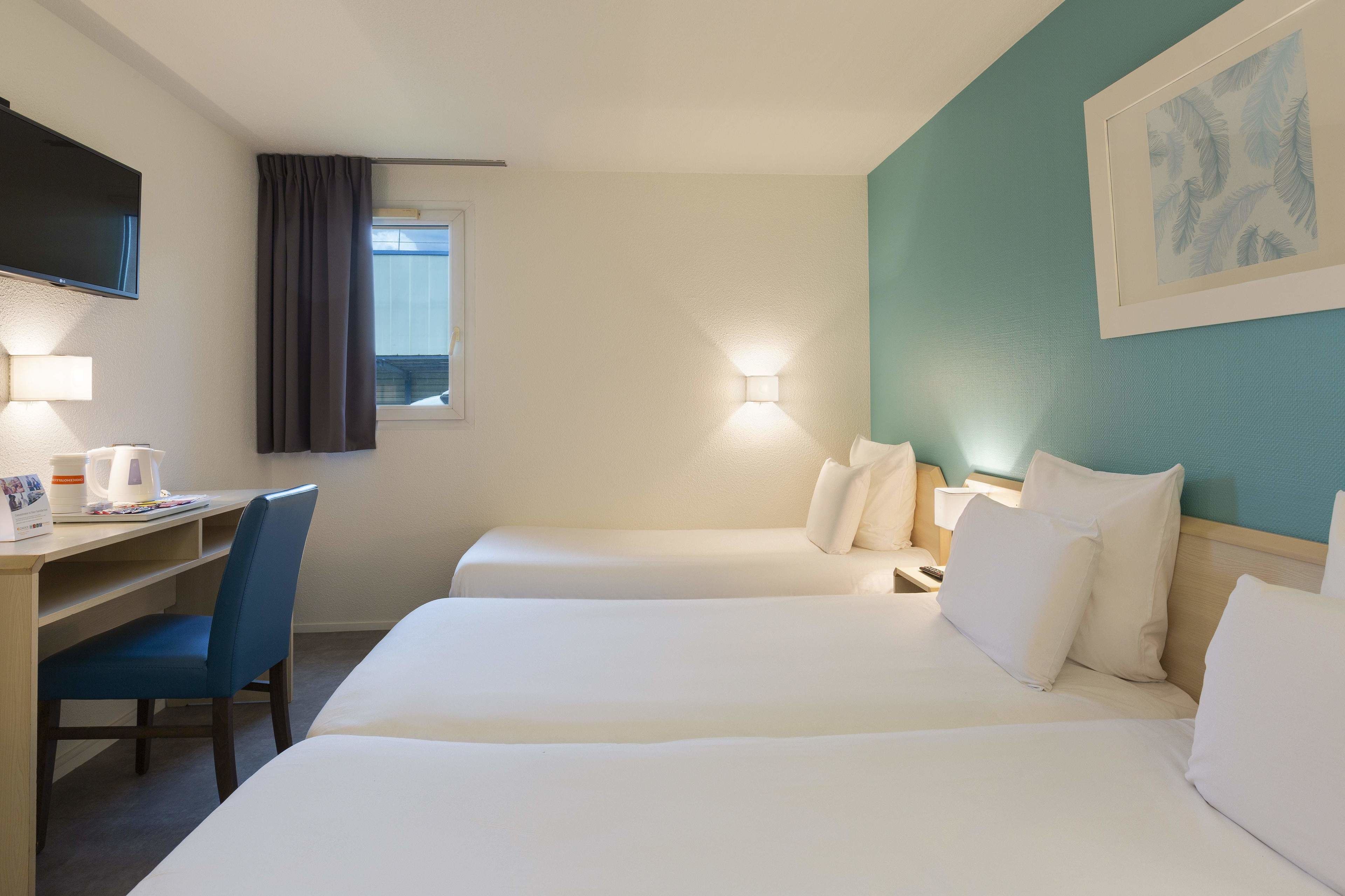 Hotelkamer met twee bedden, een bureau, een stoel, een flatscreen televisie en een raam met gordijnen.
