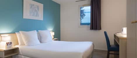 Una cama bien hecha con sábanas blancas, una mesita de noche con lámpara y un cuadro en la pared.