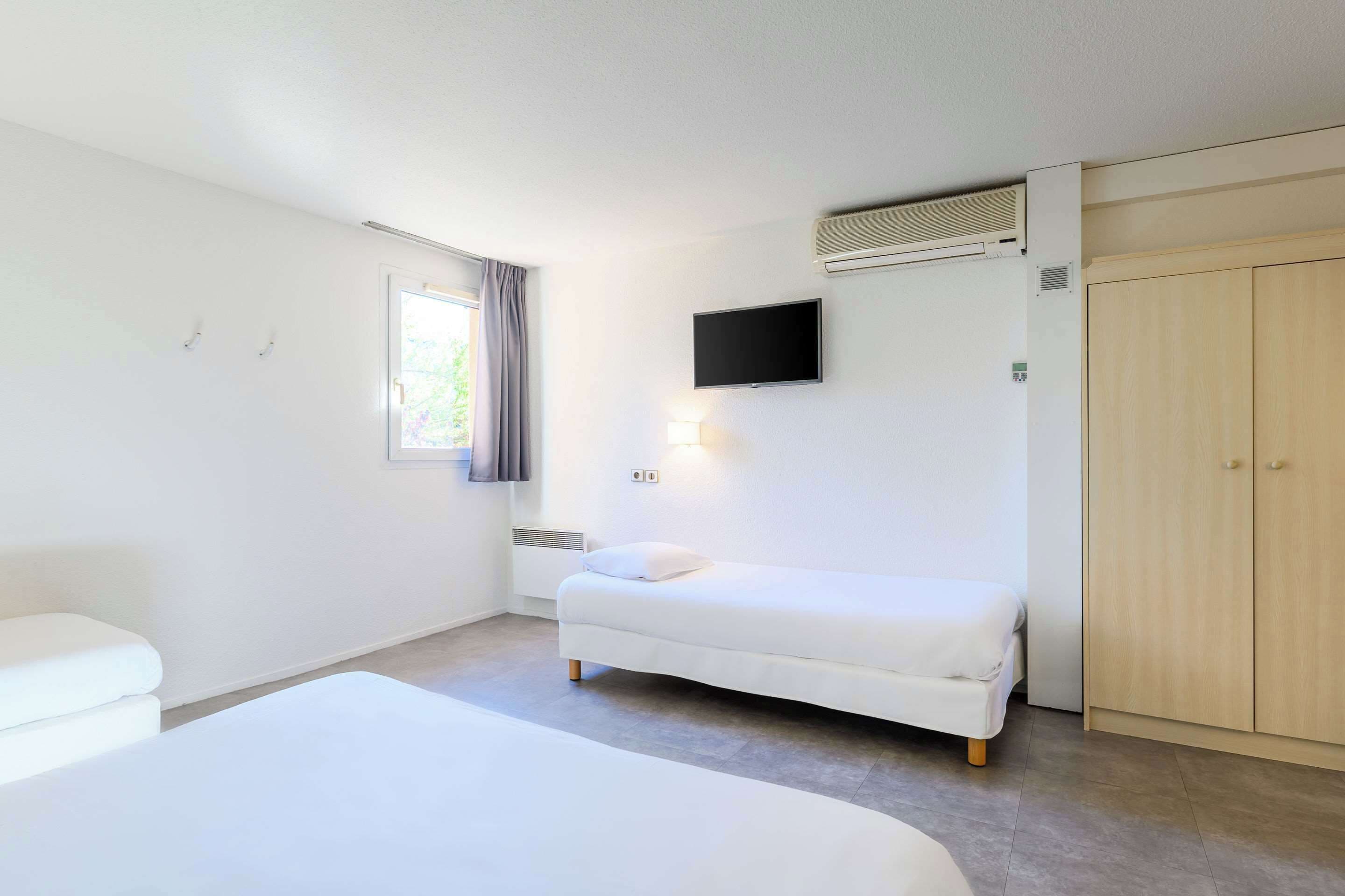Een hotelkamer met een enkel bed, een nachtkastje, een flatscreen televisie aan de muur en een garderobe.