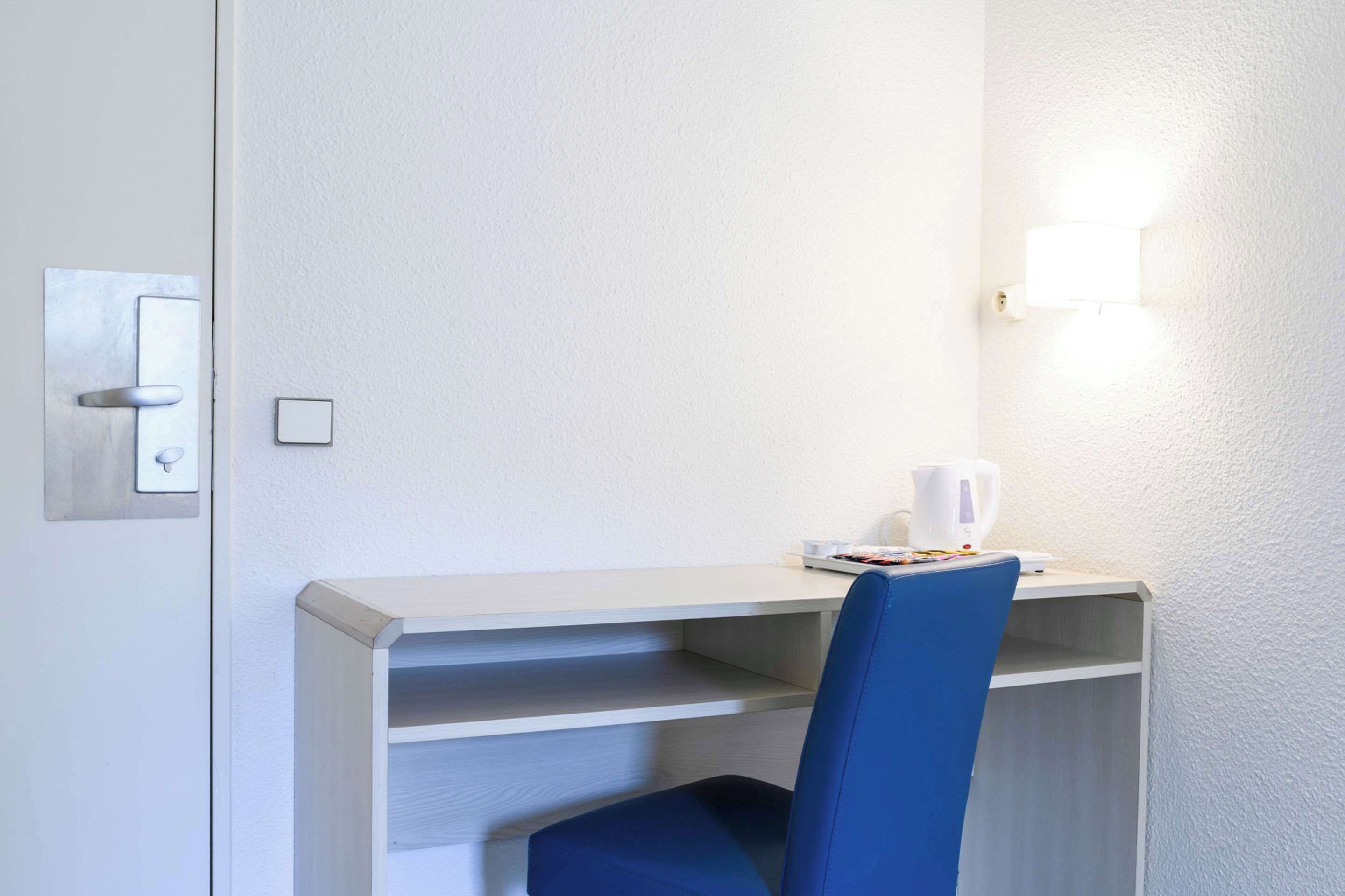 Un espacio de oficina pequeño y privado con escritorio, silla y una lámpara fijada a la pared.