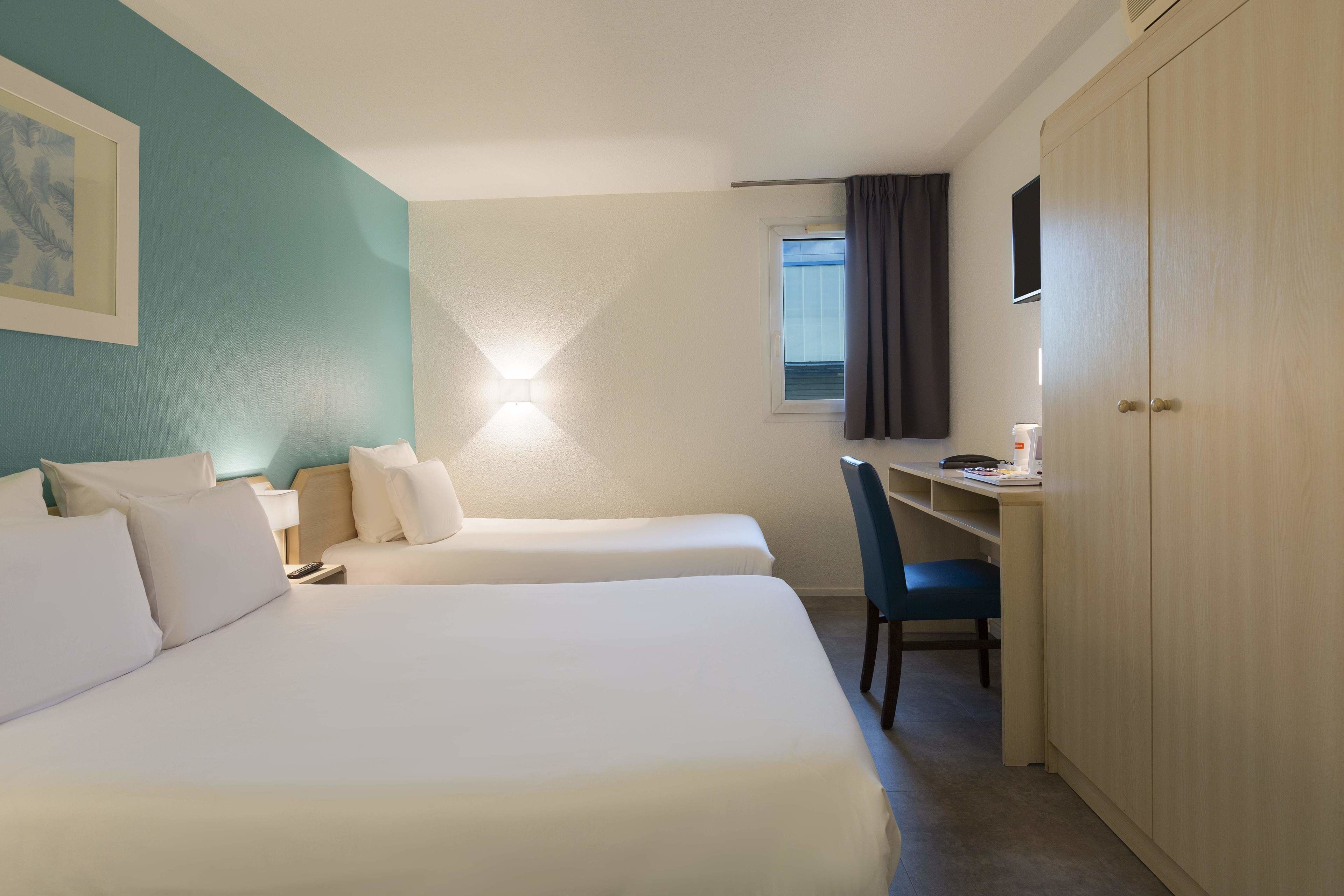 Habitación de hotel con dos camas, un escritorio, una silla, un armario y una ventana con cortinas.