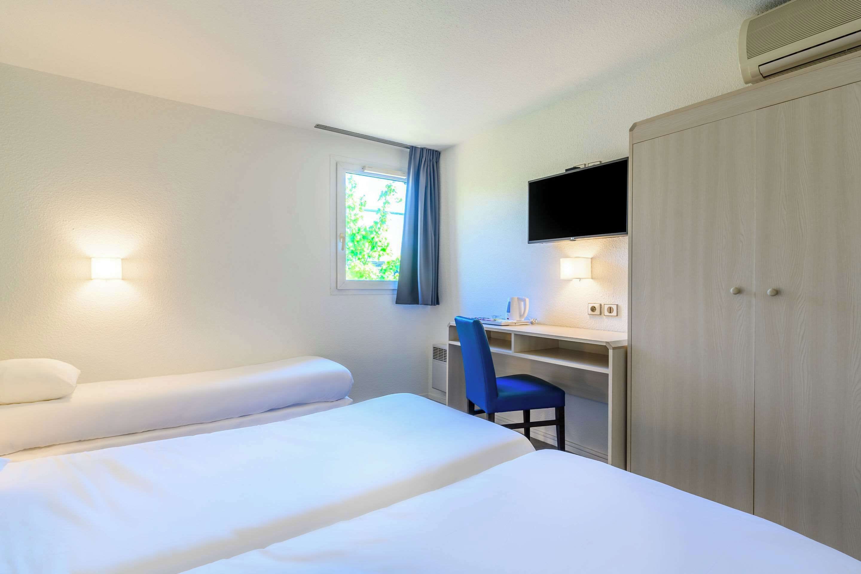 Una habitación de hotel con cama, escritorio, silla, televisor y armario.