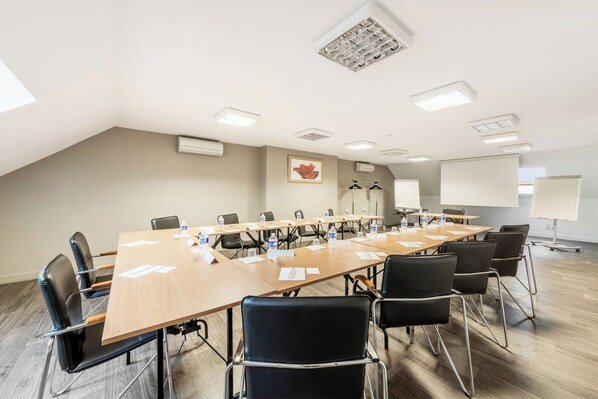 Un salón de conferencias con una larga mesa, sillas negras y una pantalla para proyector.