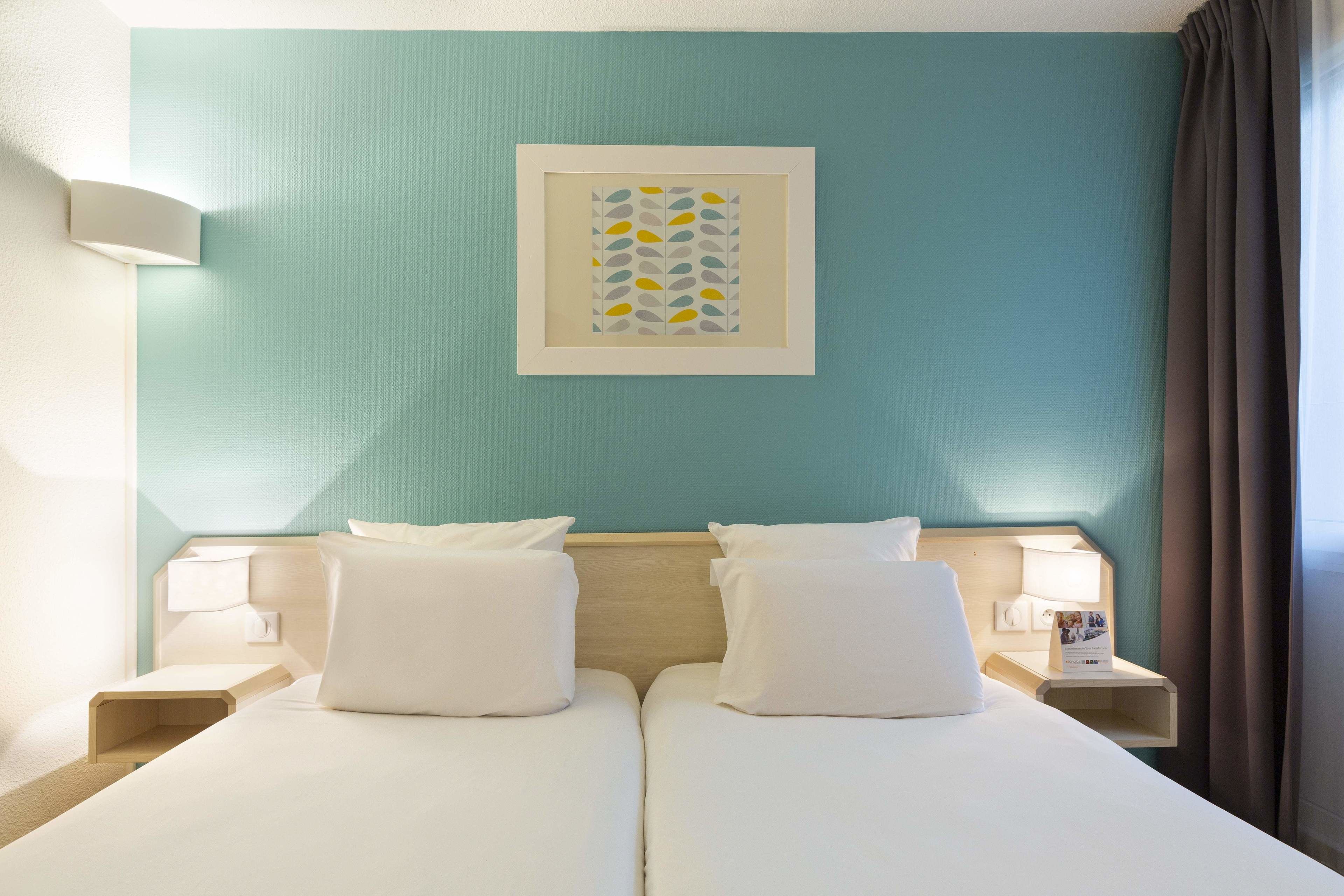 Une chambre d’hôtel avec deux lits, une œuvre d’art encadrée au mur et une table de chevet avec une lampe.