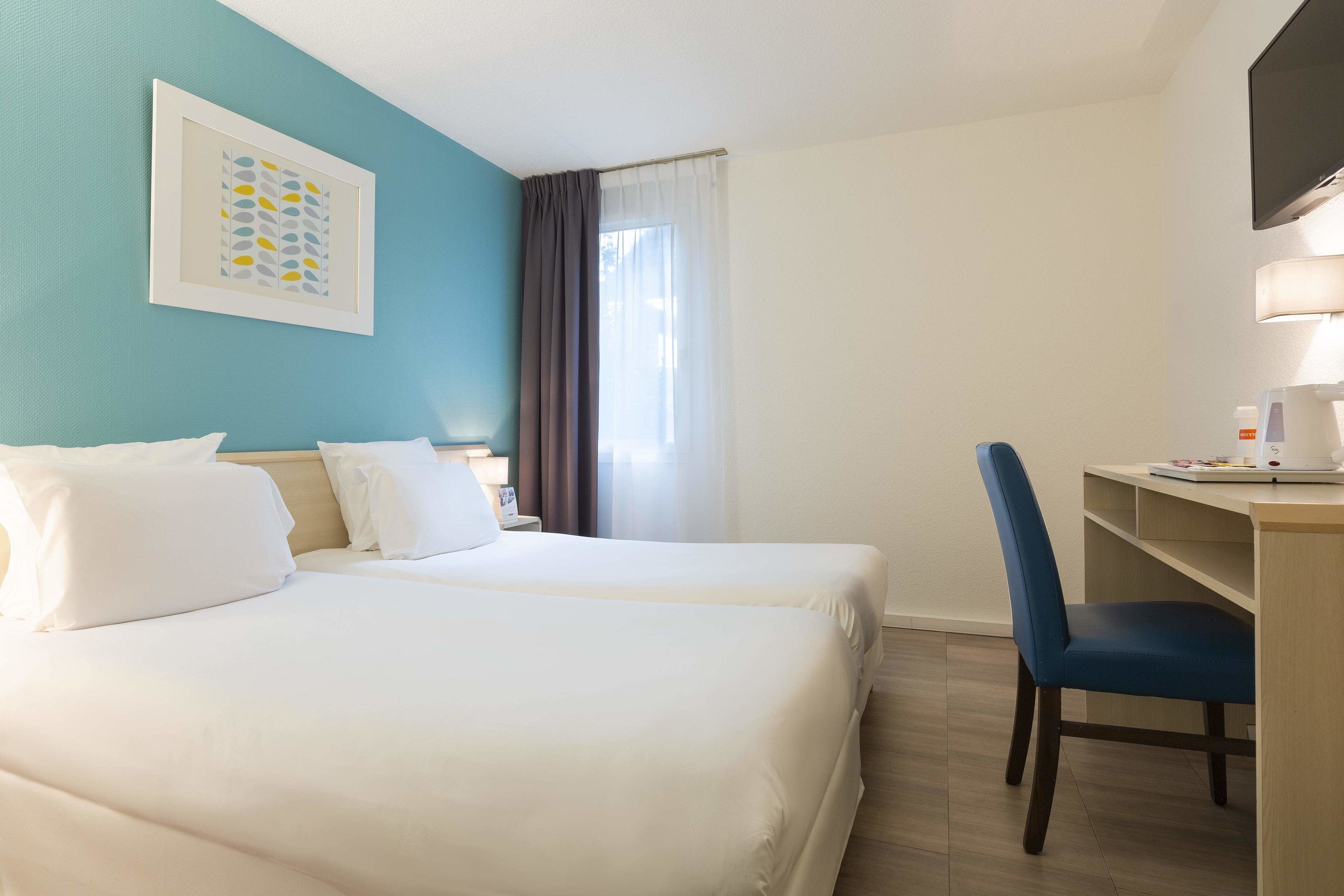 Habitación de hotel con dos camas, un escritorio, una silla, un televisor y una ventana con cortinas.