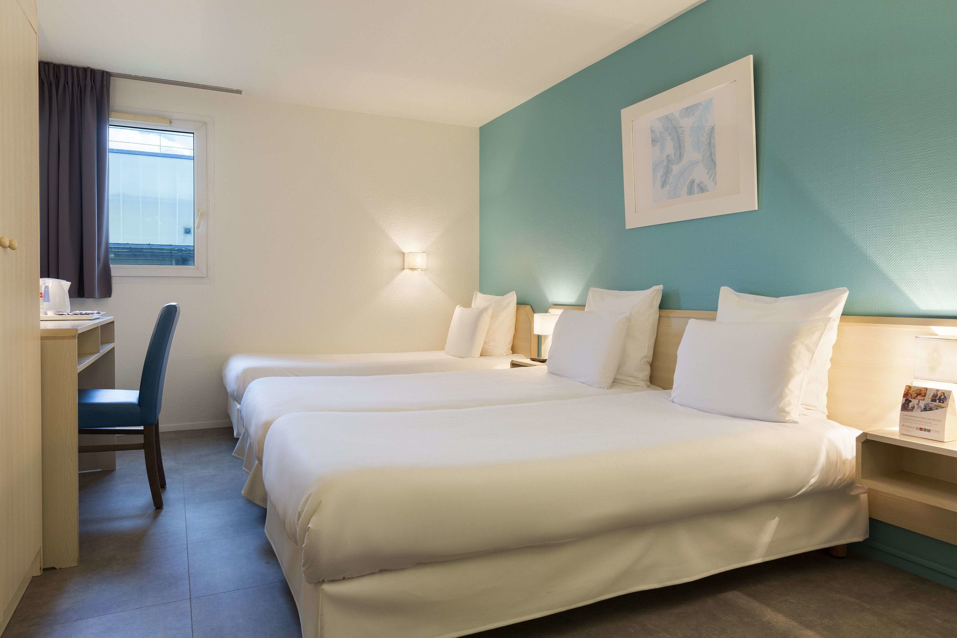 Habitación de hotel con dos camas, un escritorio, una silla y una ventana con cortinas.