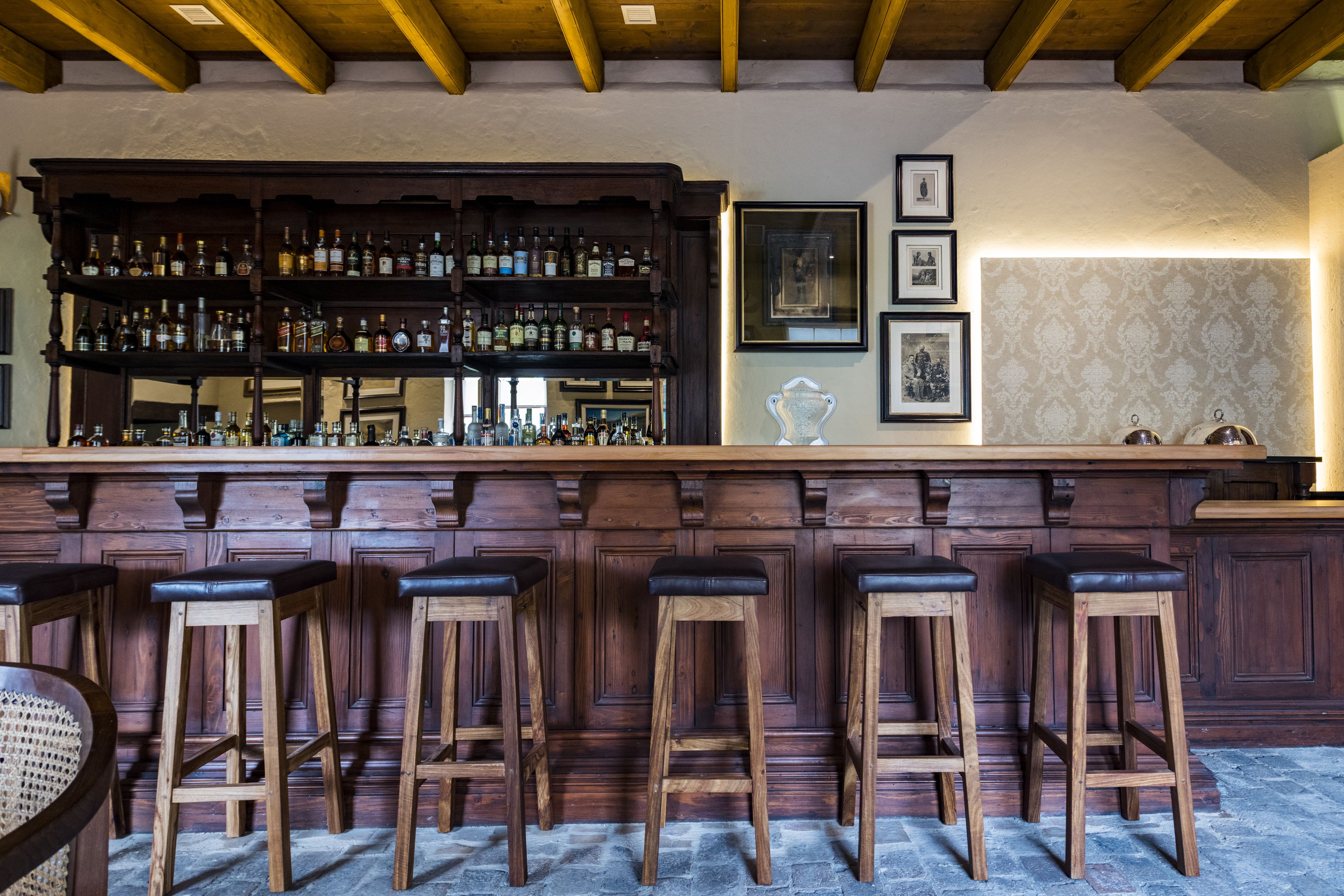 Een bar met houten krukken, een houten toog en flessenkasten vol drank.