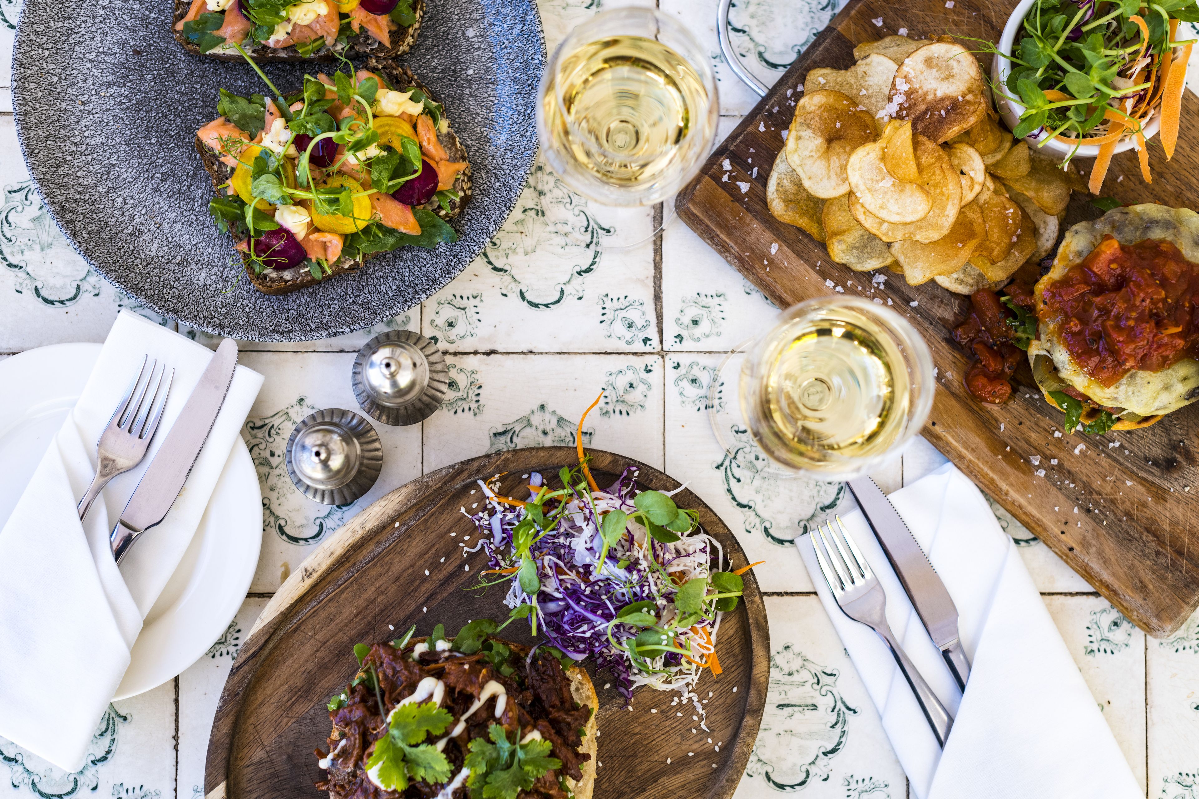Una mesa de comedor con varios platos, como una ensalada, patatas fritas y un guiso de carne, junto con copas de vino y cubiertos.