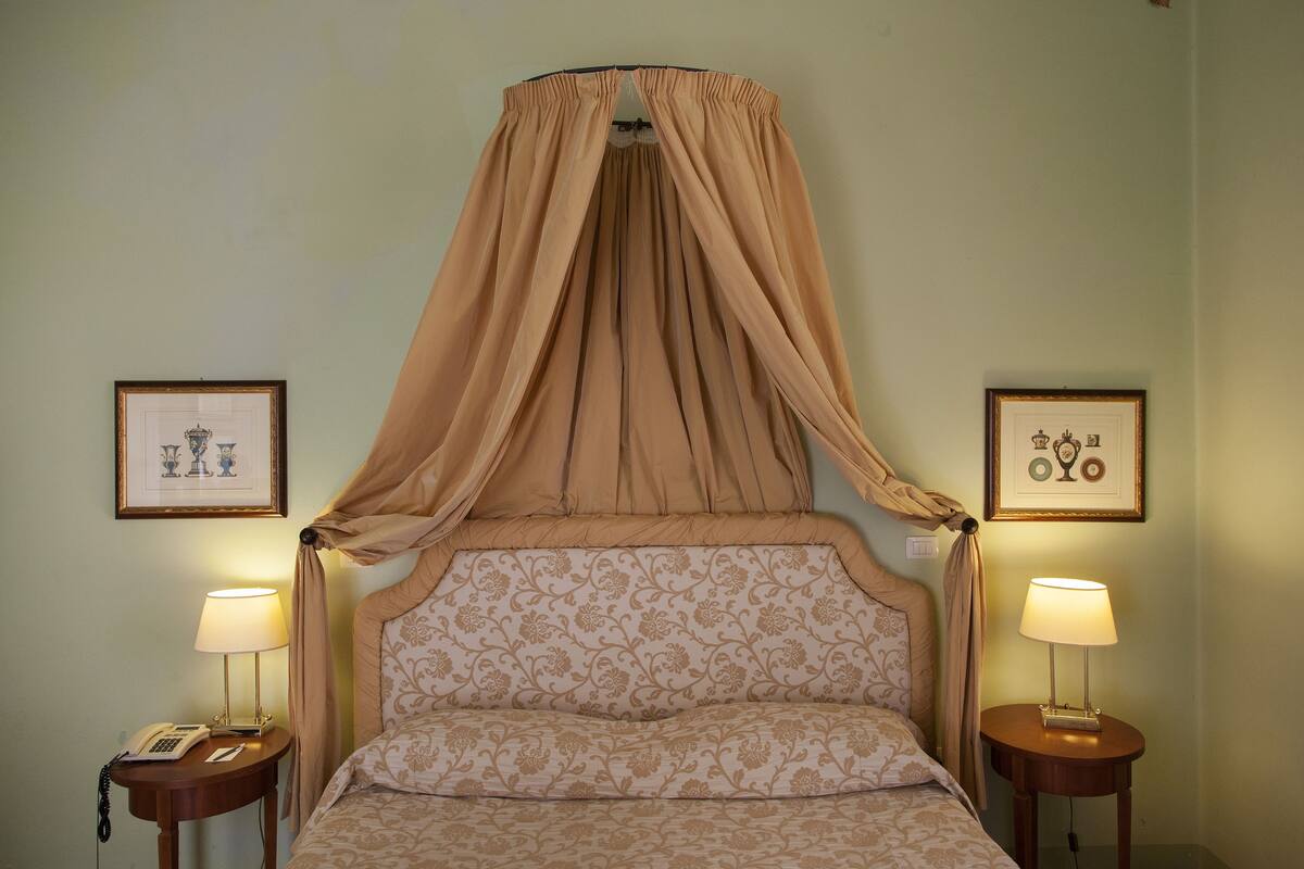 A bed with a canopy, two bedside tables with lamps, and framed pictures on the walls.