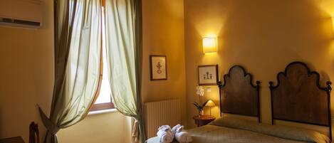 A bedroom with a bed, a window with curtains, a bedside table with a lamp, and a radiator.
