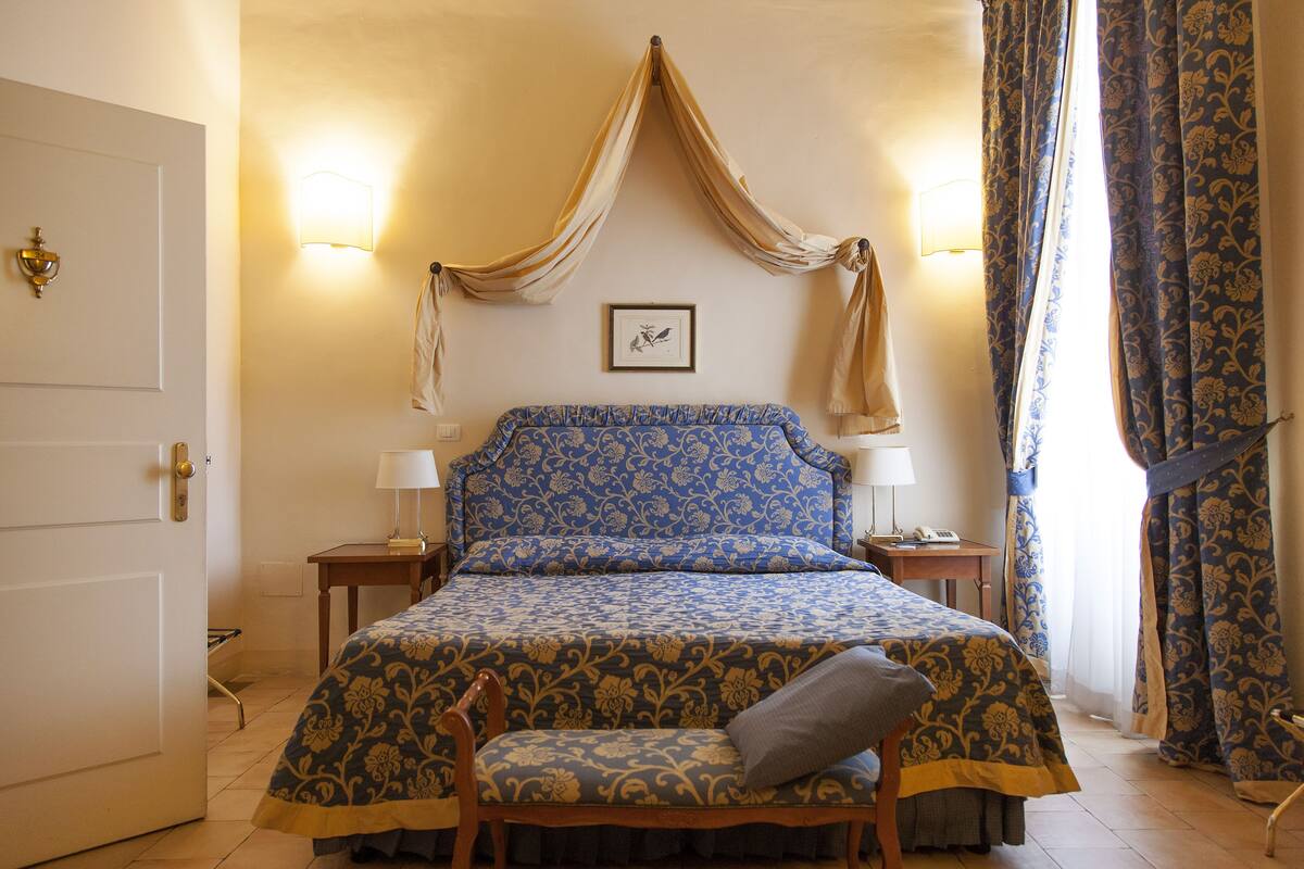 A bedroom with a bed, two bedside tables, a chair, a door, and curtains.