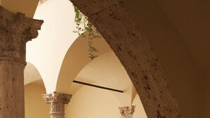 An interior courtyard with classical columns, a door, and potted plants. - Palazzo Guiderocchi (Ascoli Piceno)