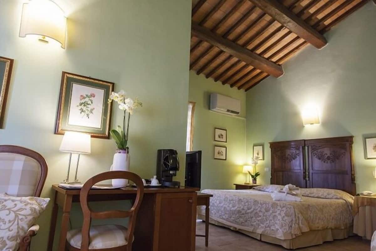 A hotel room with a wooden ceiling, a bed with a floral bedspread, a desk with a chair, and a small table with a lamp.