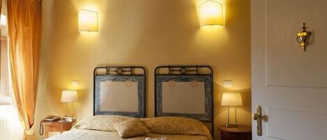Habitación de hotel con dos camas, cada una con cabecero y lámparas de noche. Se ve una puerta a la derecha de la imagen.