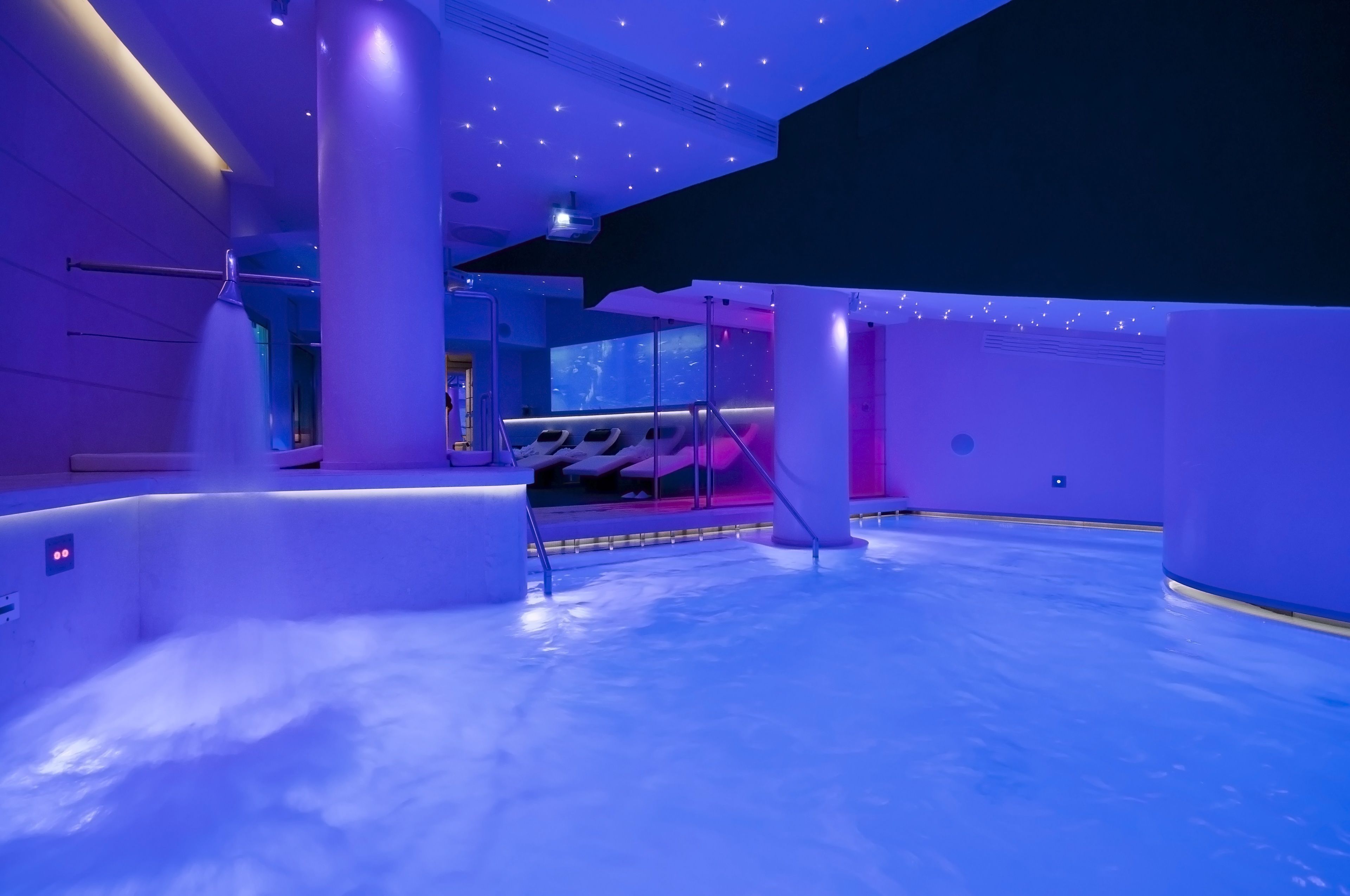 A modern spa area with a large pool, seating area, and a ceiling with star-like lights.