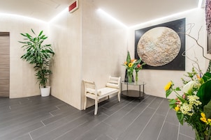 Un'area reception con una panca, piante in vaso, un tavolo rotondo e un grande quadro astratto.