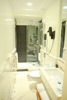 Un bagno stretto con cabina doccia in vetro, un water e un lavandino con specchio.