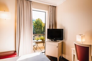 Una camera d'albergo con un letto, una televisione su un mobile, una sedia e vista su un balcone con tavolo e sedie.