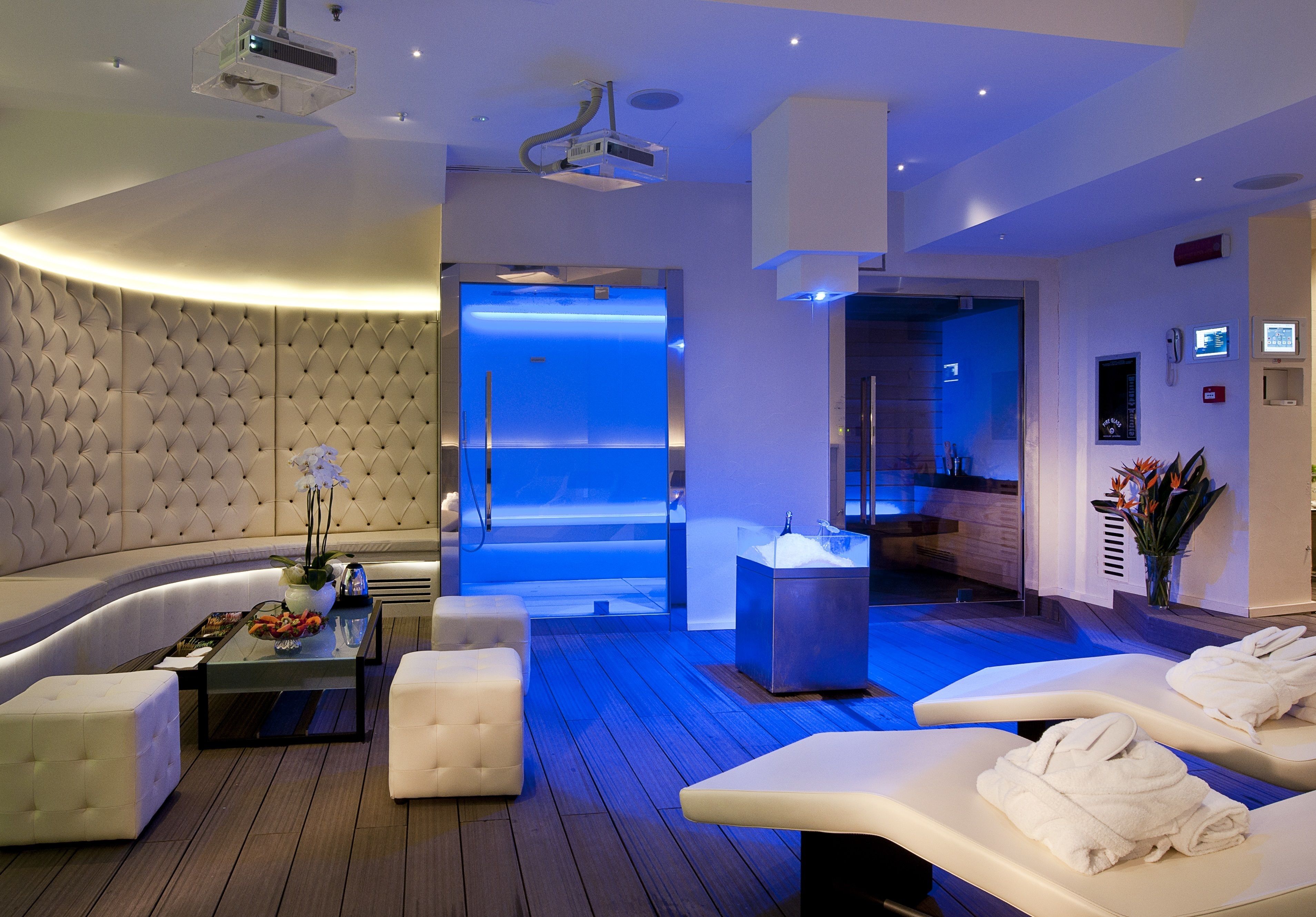 Un moderno salón de spa con una zona de asientos curvos, una camilla de masaje y un espacio de relajación con iluminación azul.