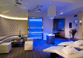 Una moderna stanza spa con un'area salotto a forma di curva, un lettino da massaggio e una zona relax illuminata di blu.
