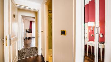 Un pasillo de hotel con piso de madera, pared roja y una puerta blanca que da a un baño con ducha y retrete.