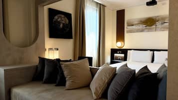 Habitación de hotel con sofá, cama con almohadas, mesita de noche, lámpara, un cuadro y un proyector en el techo.