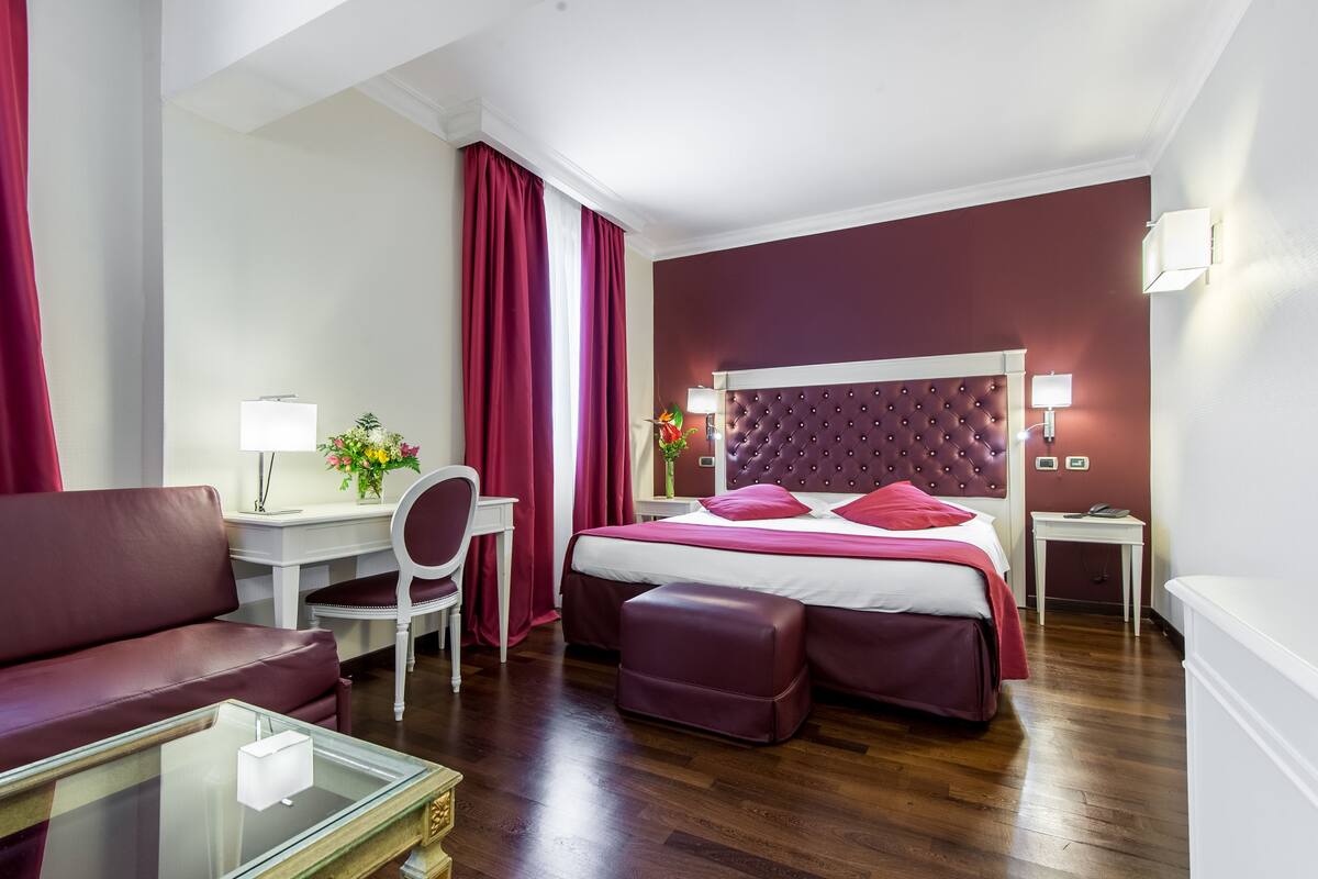 A hotel room with a bed, a desk, a chair, a sofa, and a small table.