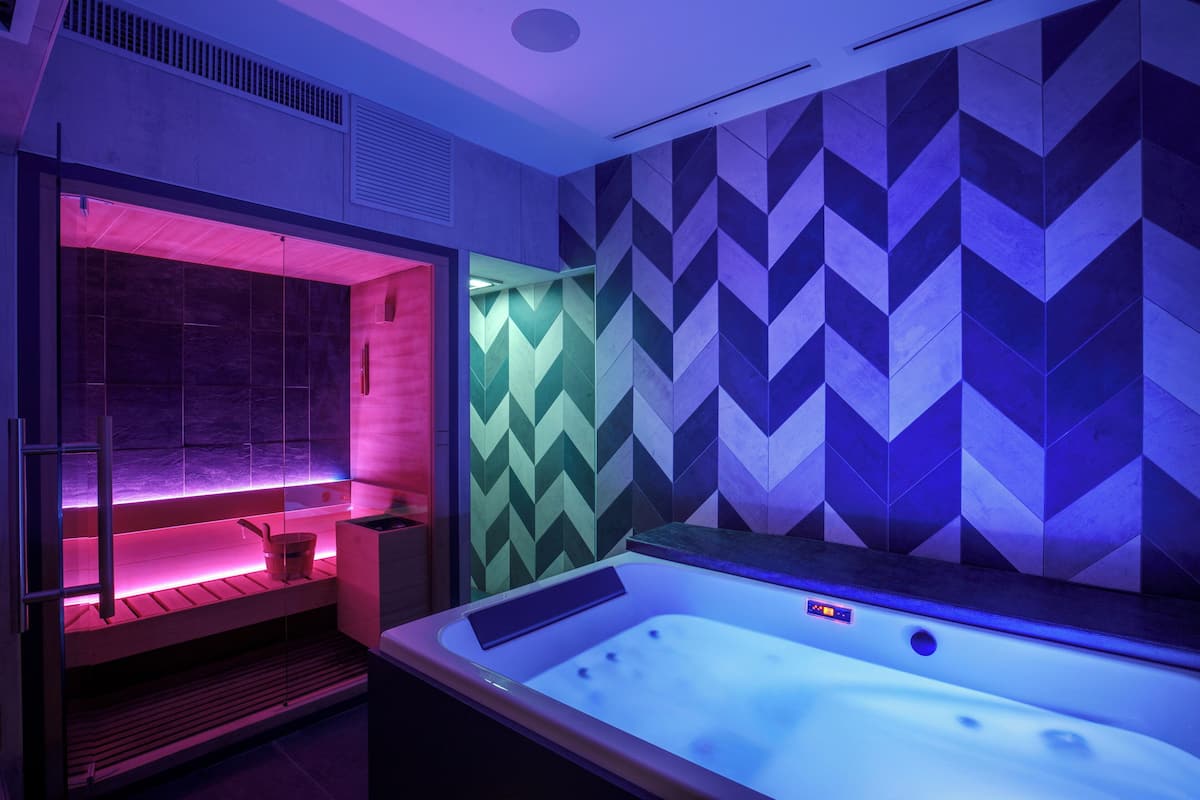 A modern spa room with a heated tub, a steam shower, and a wooden bench.