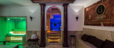 A lobby with a green-lit massage room, a staircase leading to a blue-lit area, and a seating area with a mural.