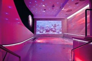 Un'elegante spa con un grande schermo che mostra una scena subacquea, illuminazione soffusa e un design moderno.