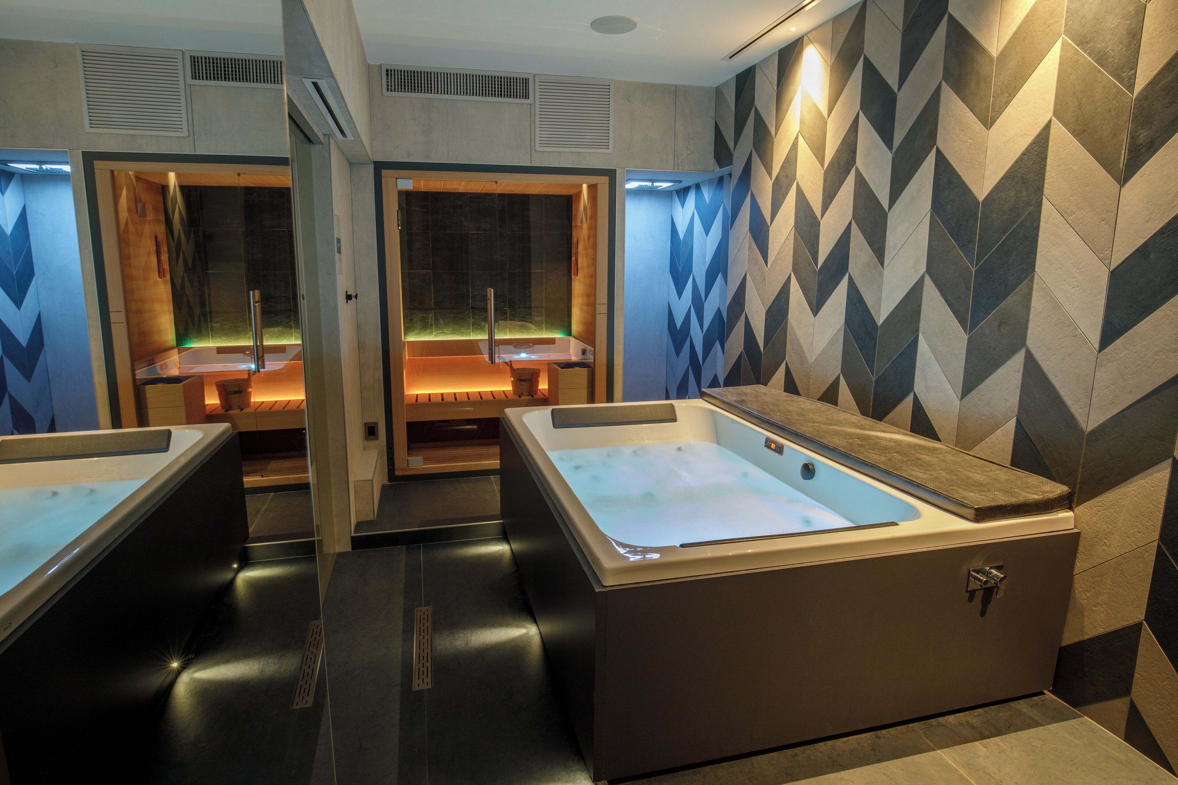 Une salle de bain moderne avec deux grandes baignoires, un banc en bois et un mur orné de motifs.