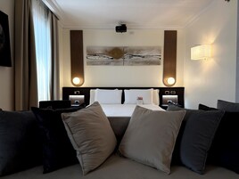 Una camera d'albergo con un letto grande, due comodini, un proiettore a soffitto, un'opera d'arte appesa al muro e un punto luce a parete.