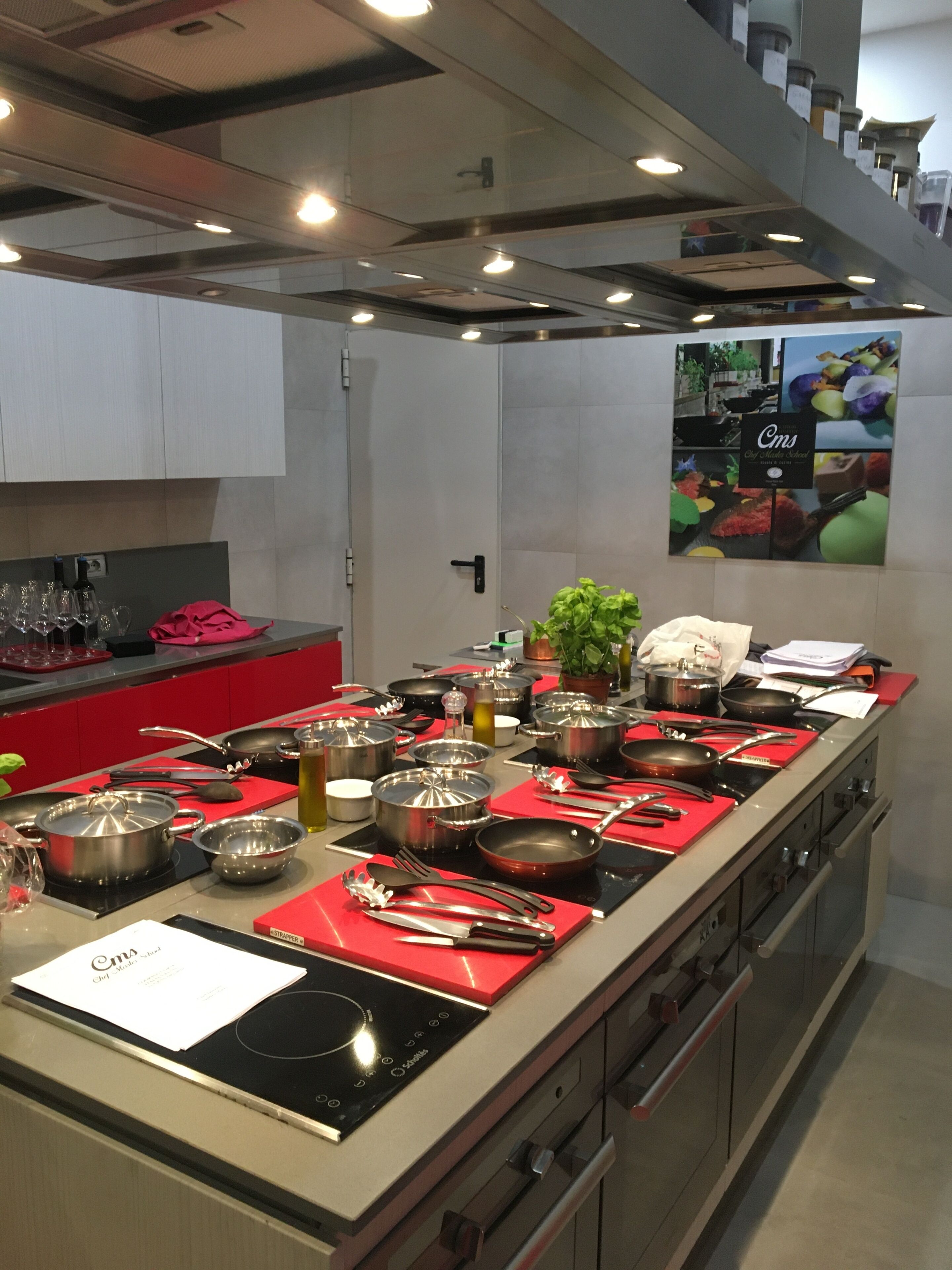 A modern kitchen with stainless steel appliances, red countertops, and a variety of cookware.